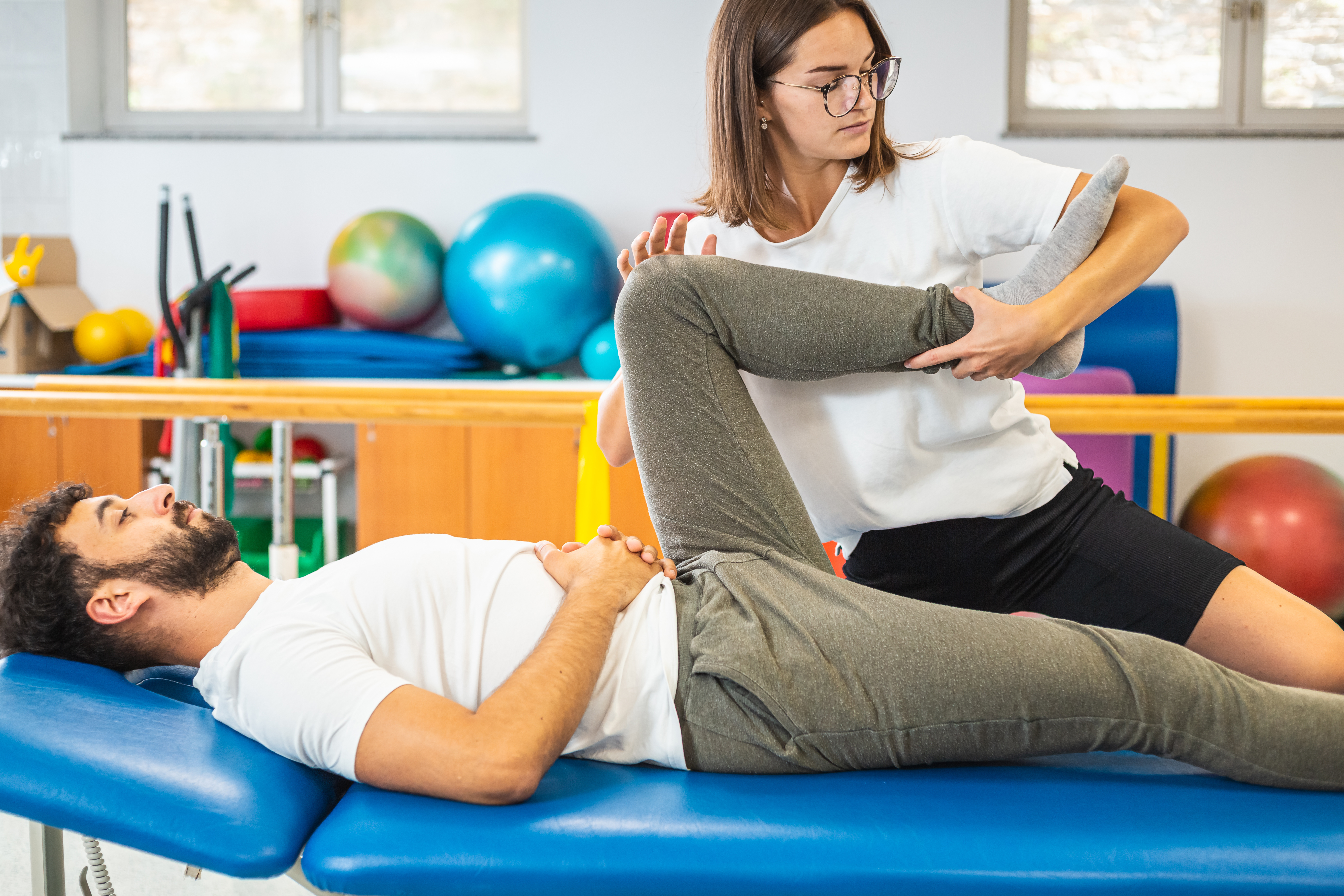 Woman physiotherapist giving a rehabilitation leg and hip treatment to a male patient.
