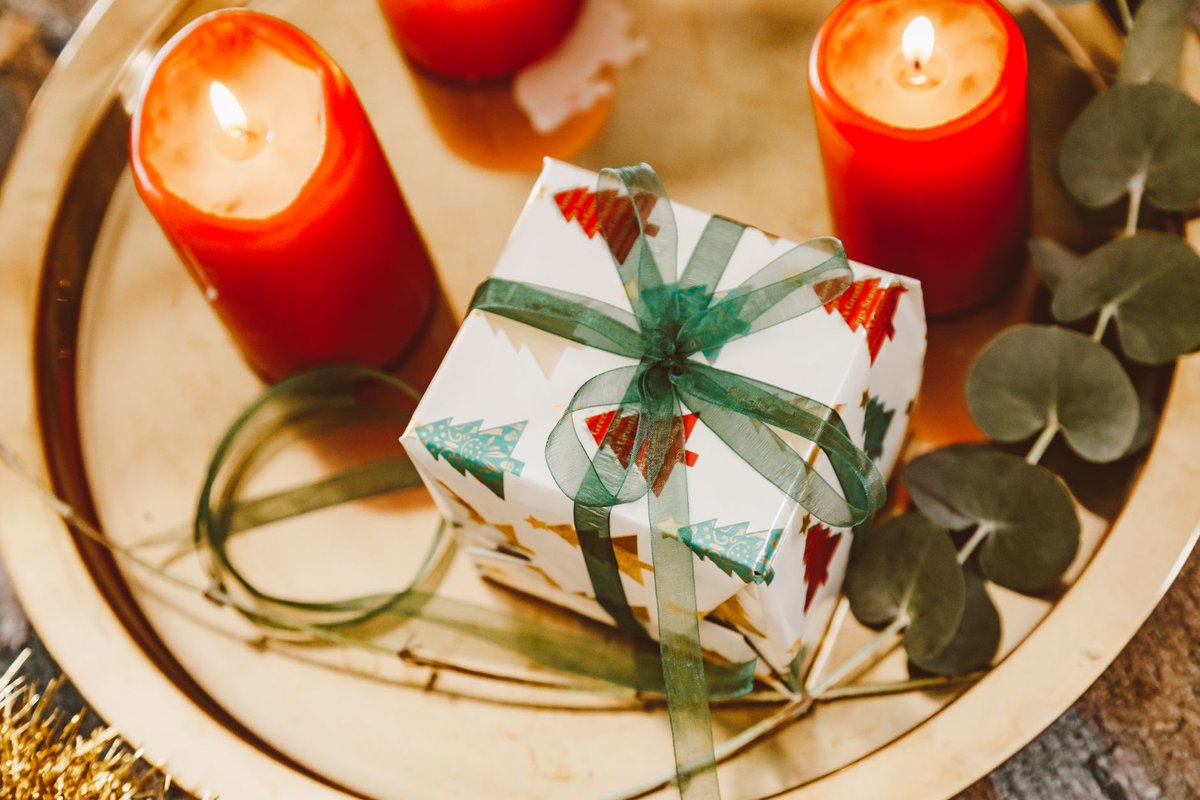 Top view of a wrapped Christmas gift on a tray with candles and eucalyptus.