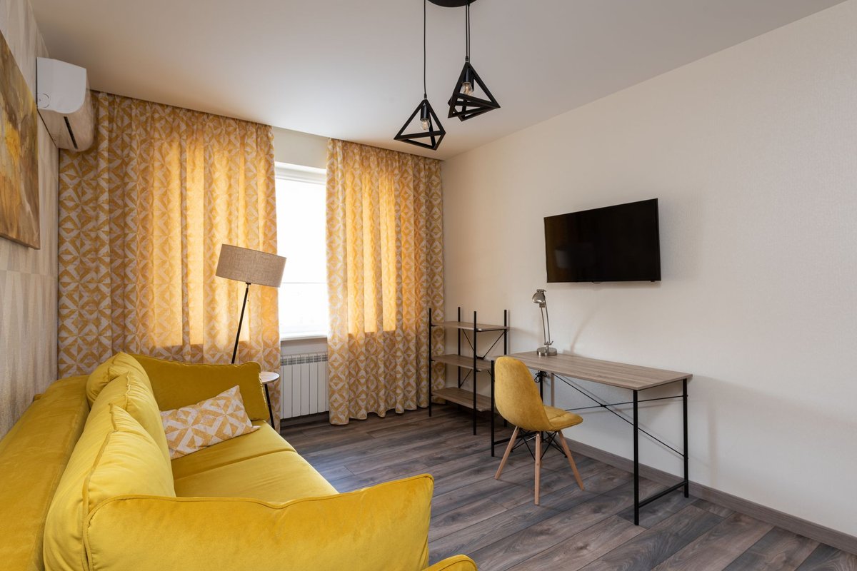 Interior of modern living room in yellow colors with TV set sofa pillows table and curtains