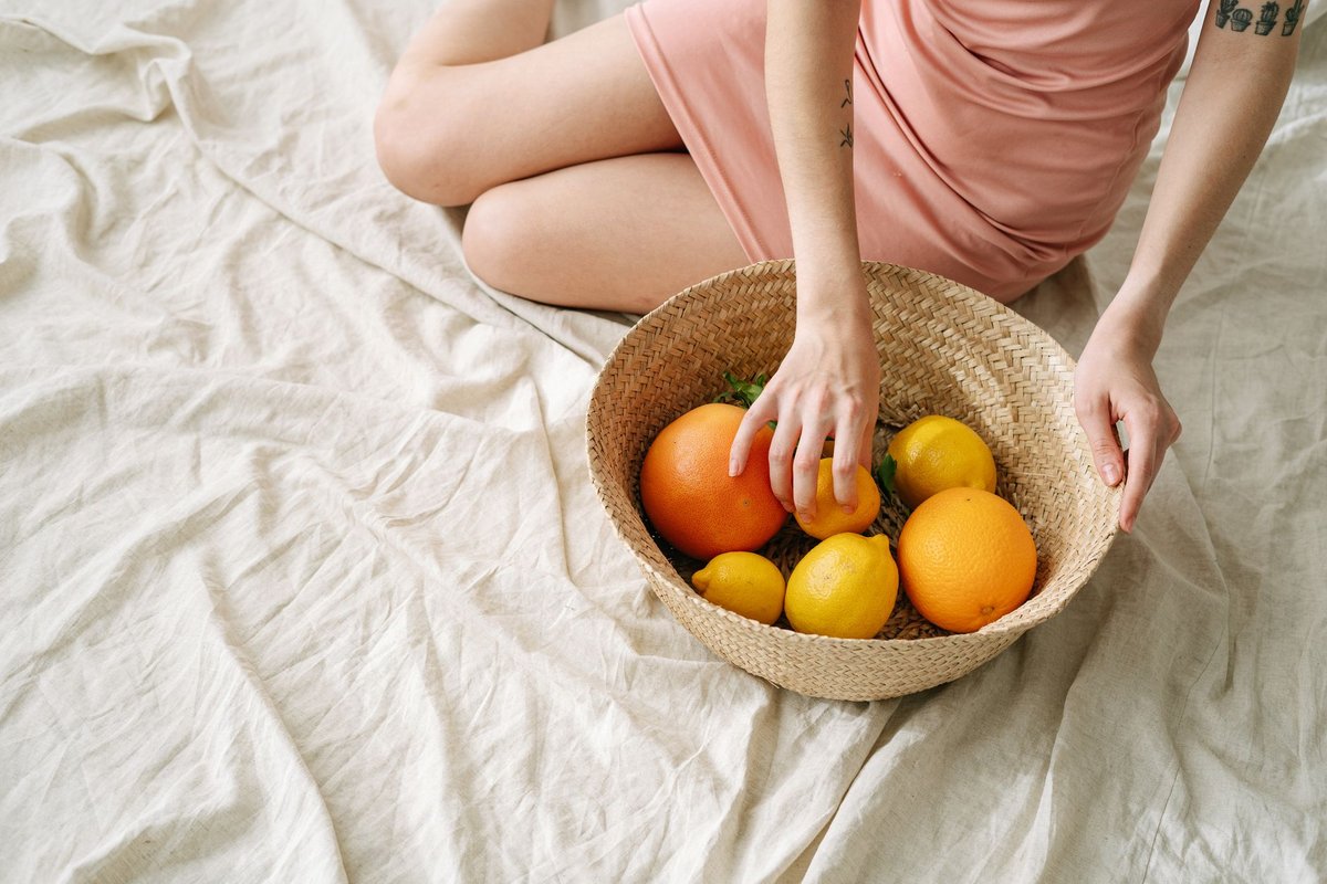 A woman in a pink dress holding a basket of fresh citrus fruits, including oranges and lemons.