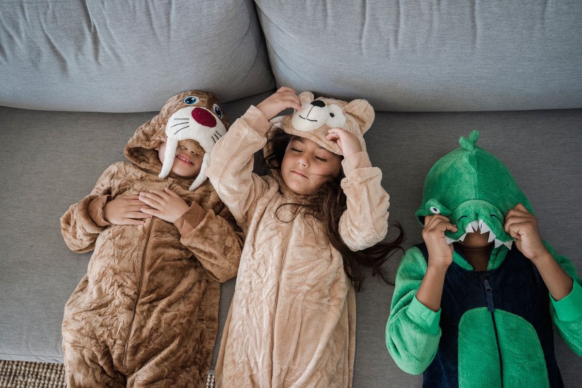 Three kids wearing animal costumes playing together on a sofa, enjoying fun and laughter.