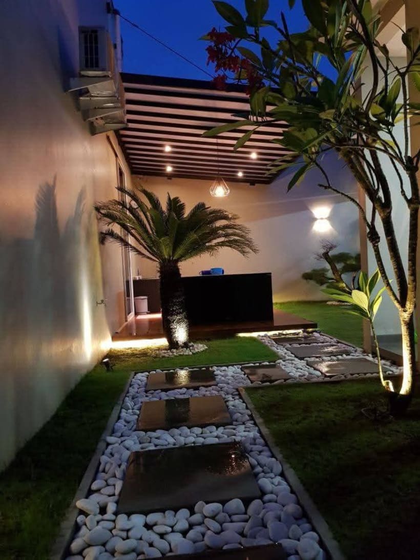 Terraza moderna con camino de piedras y vegetación iluminada