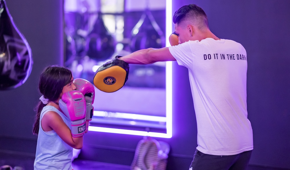 young girl wearing boxing gloves working with a man holding punching mitts