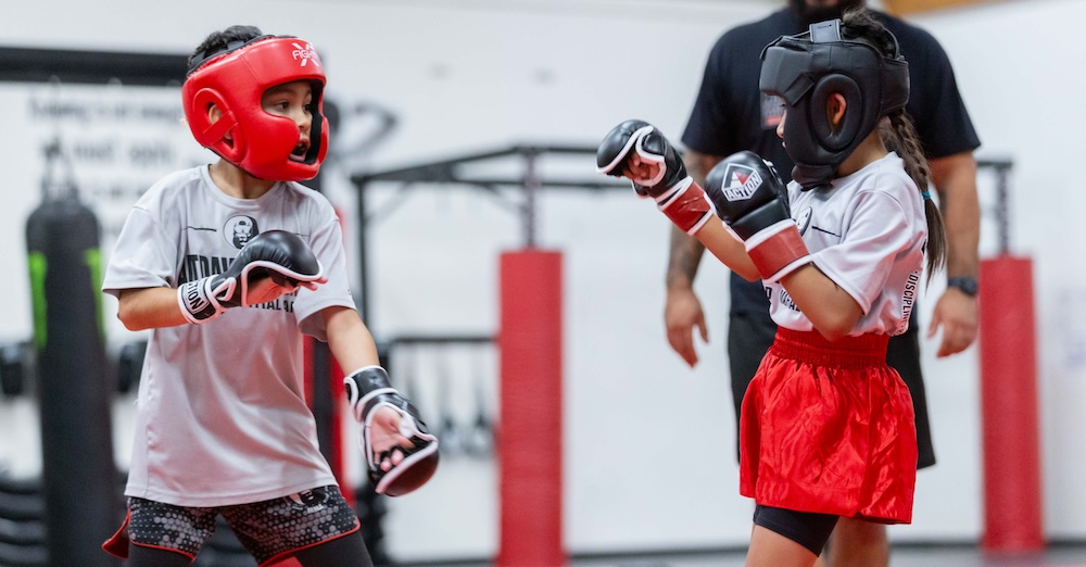 two kids with boxing gloves and headgear in a MMA class