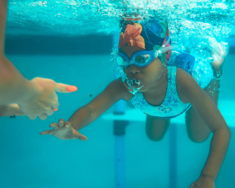 Swim instructor guiding a young swimmer underwater in a bright blue pool
