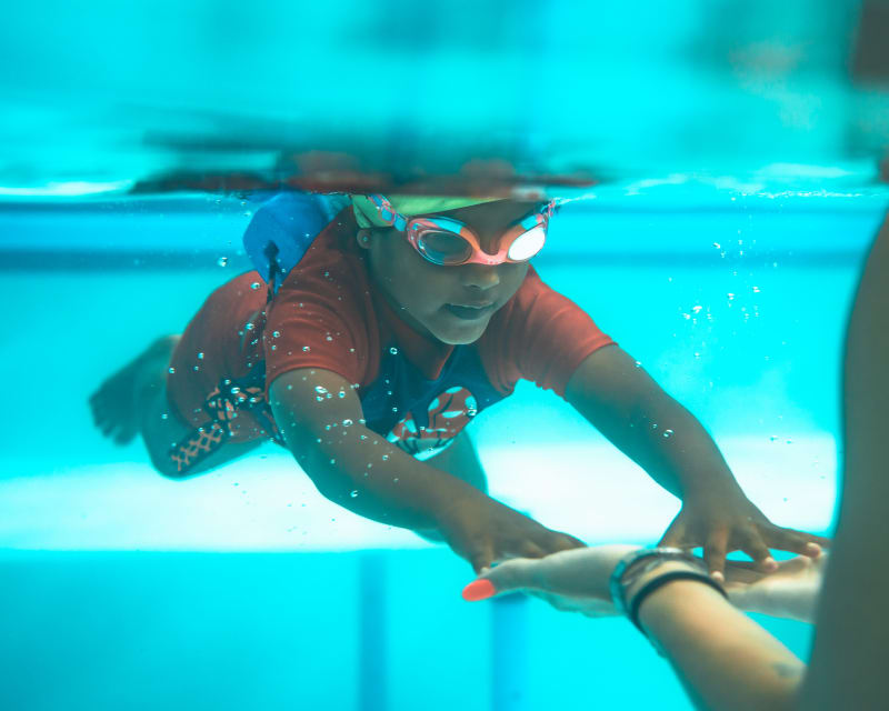 Young swimmer in goggles kicking forward underwater during a swim lesson