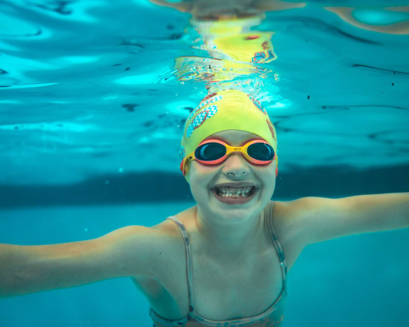 Smiling young swimmer in a yellow cap and goggles underwater in a pool