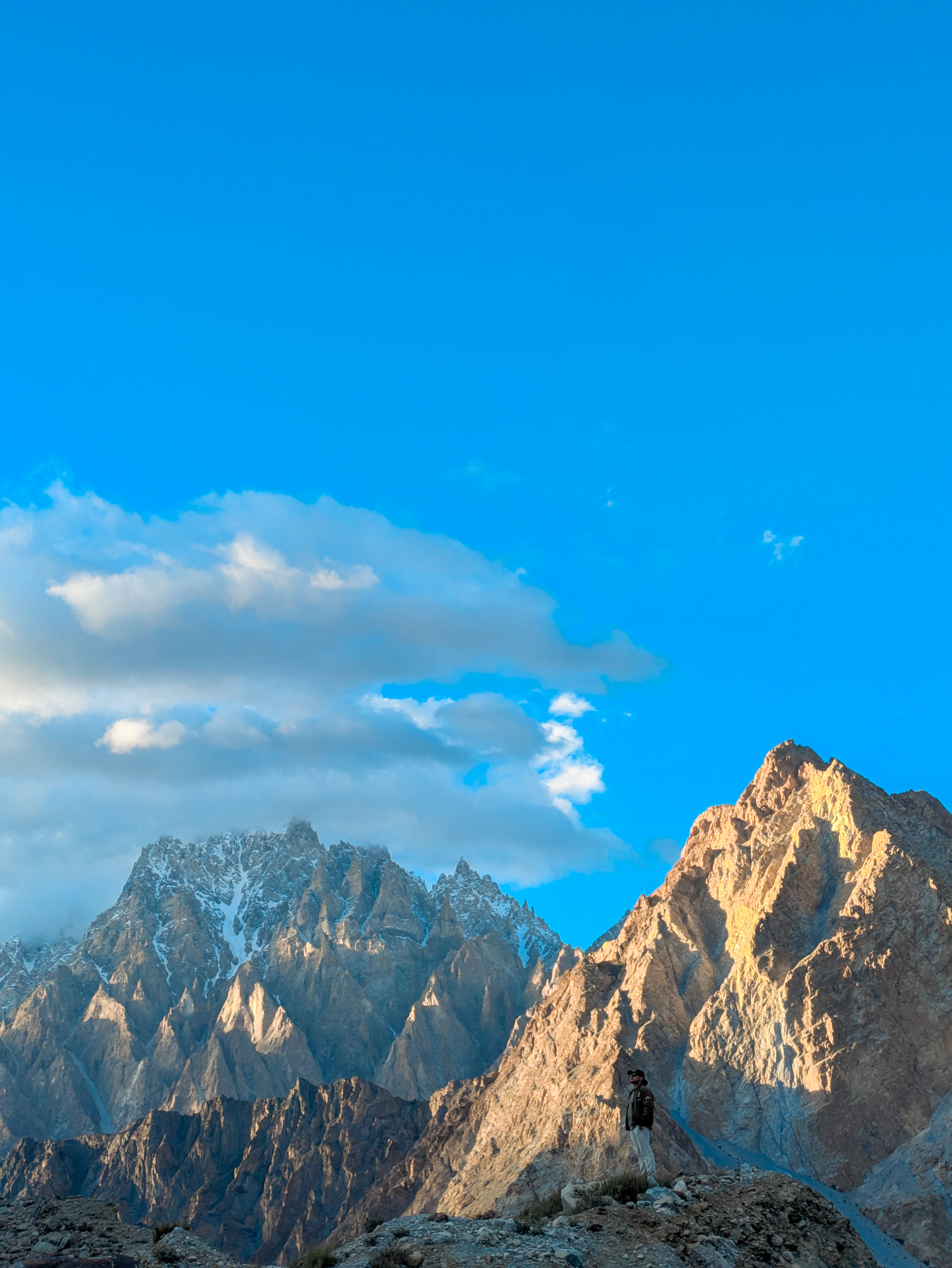 Samie Ullah Baig standing on a cliff with the Passu Cones in the background.