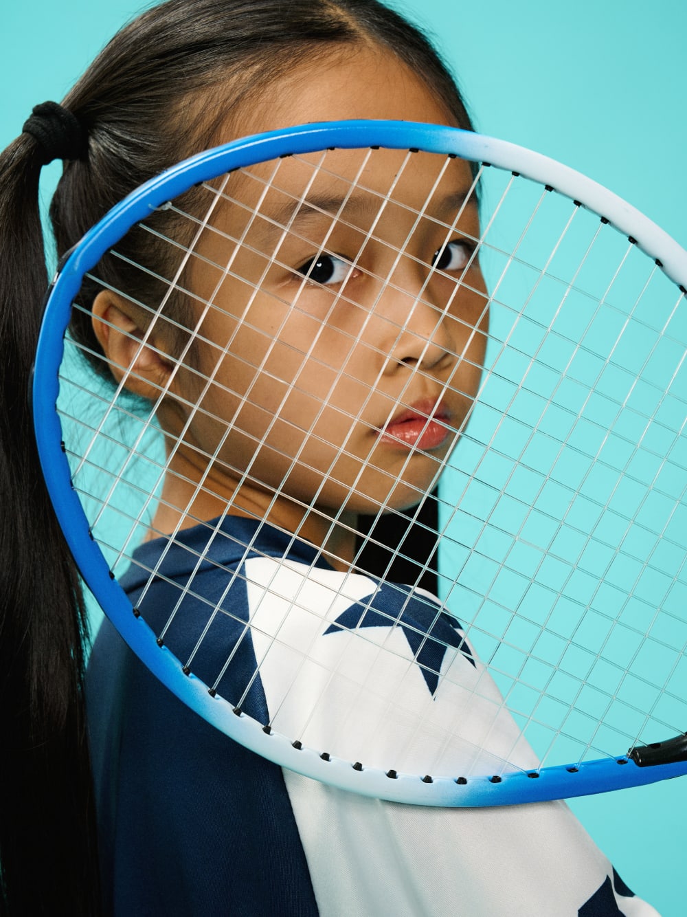 Face seen through the strings of a raised tennis racket.