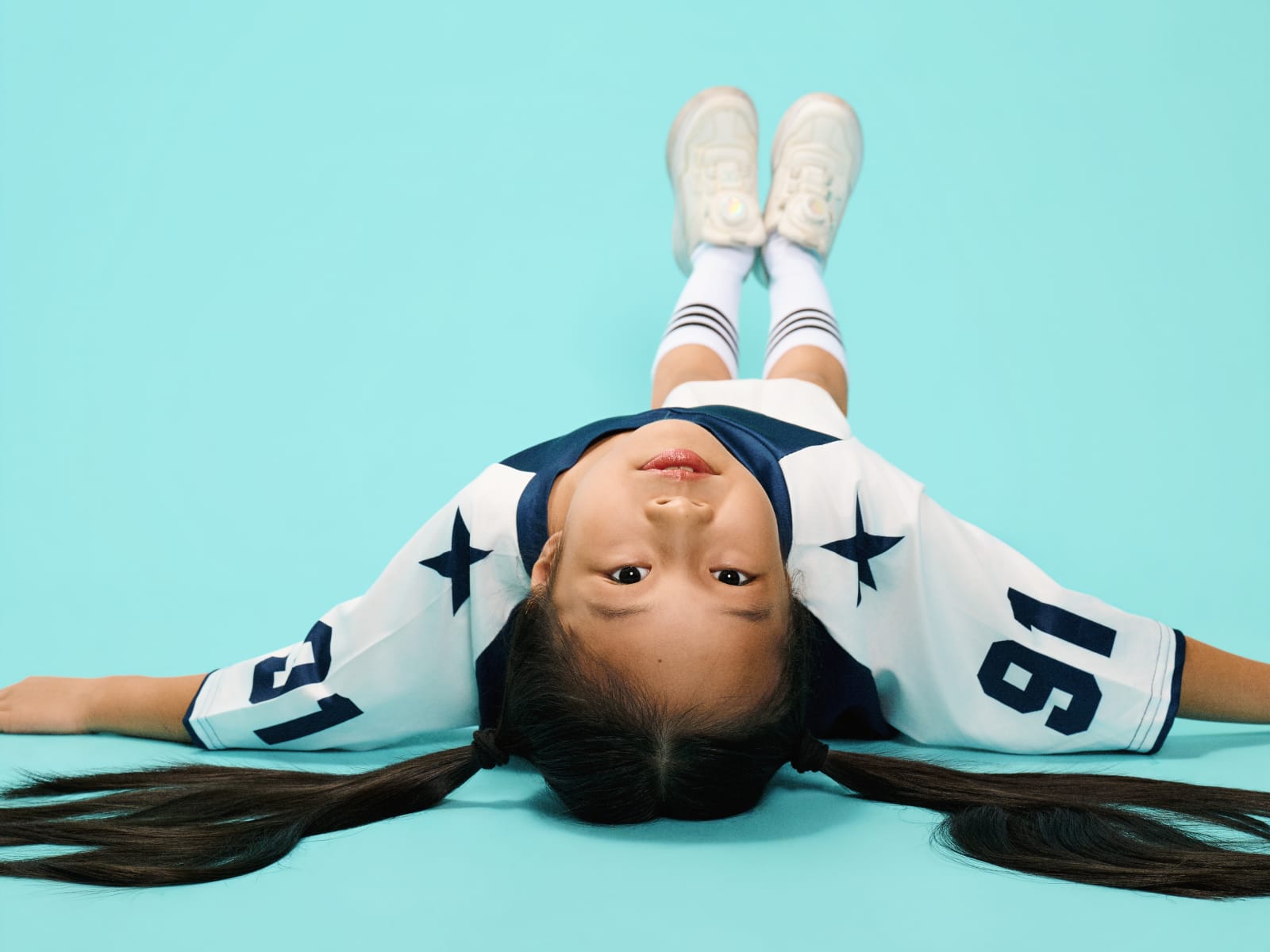 Lying back with hair fanned out, sneakers up, shot from above.