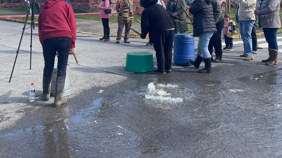 Vecinos de Entre Lagos junto a un afloramiento de agua en la calzada del sector General Lagos, con cinta de peligro y bidones