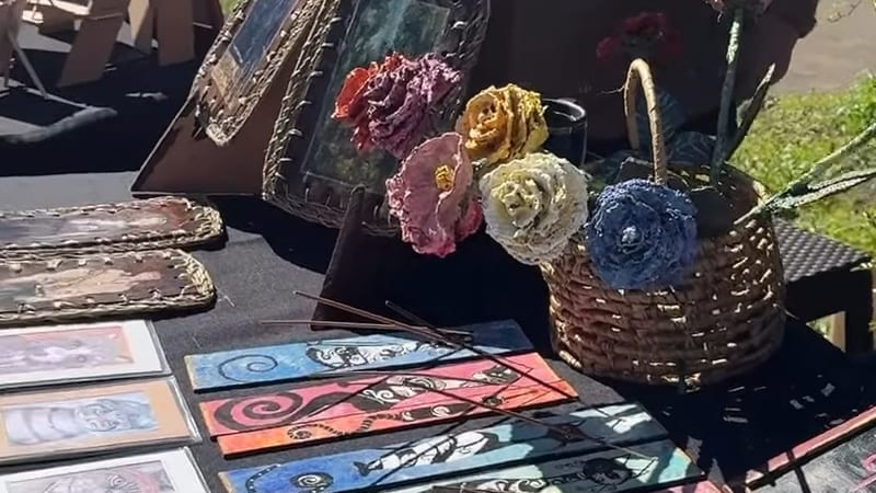 Obras de pequeño formato, cuadros enmarcados y flores textiles sobre una mesa en la exposición Cultura Viva, en la costanera de Frutillar Bajo