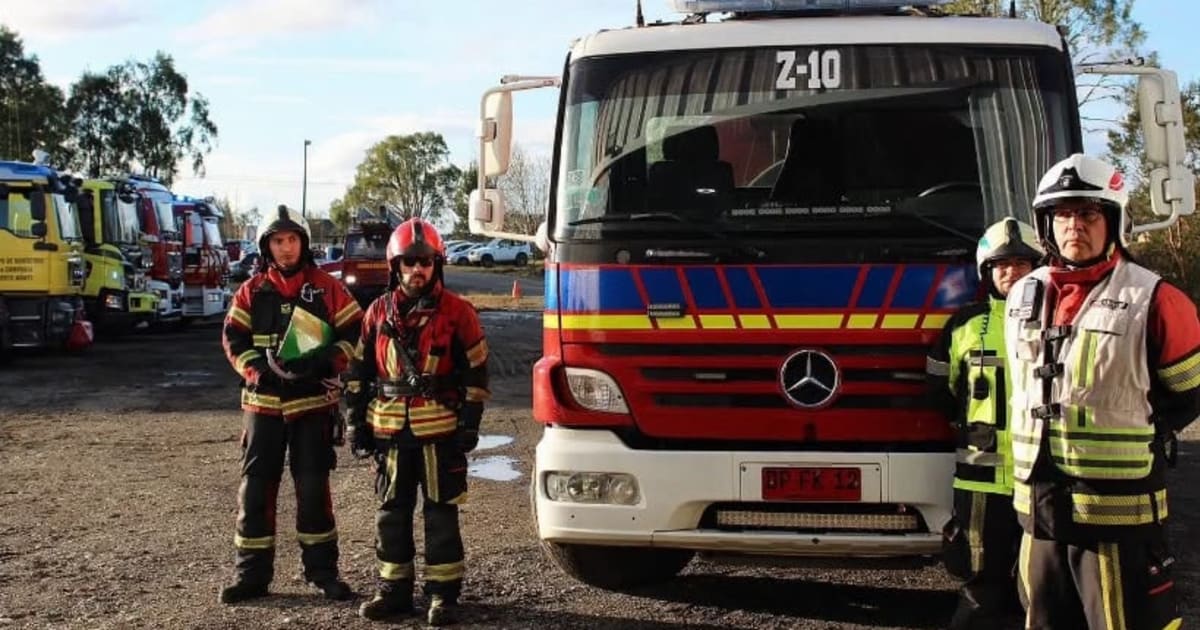 Voluntarios de bomberos junto a un carro cisterna estacionado, con otros carros al fondo