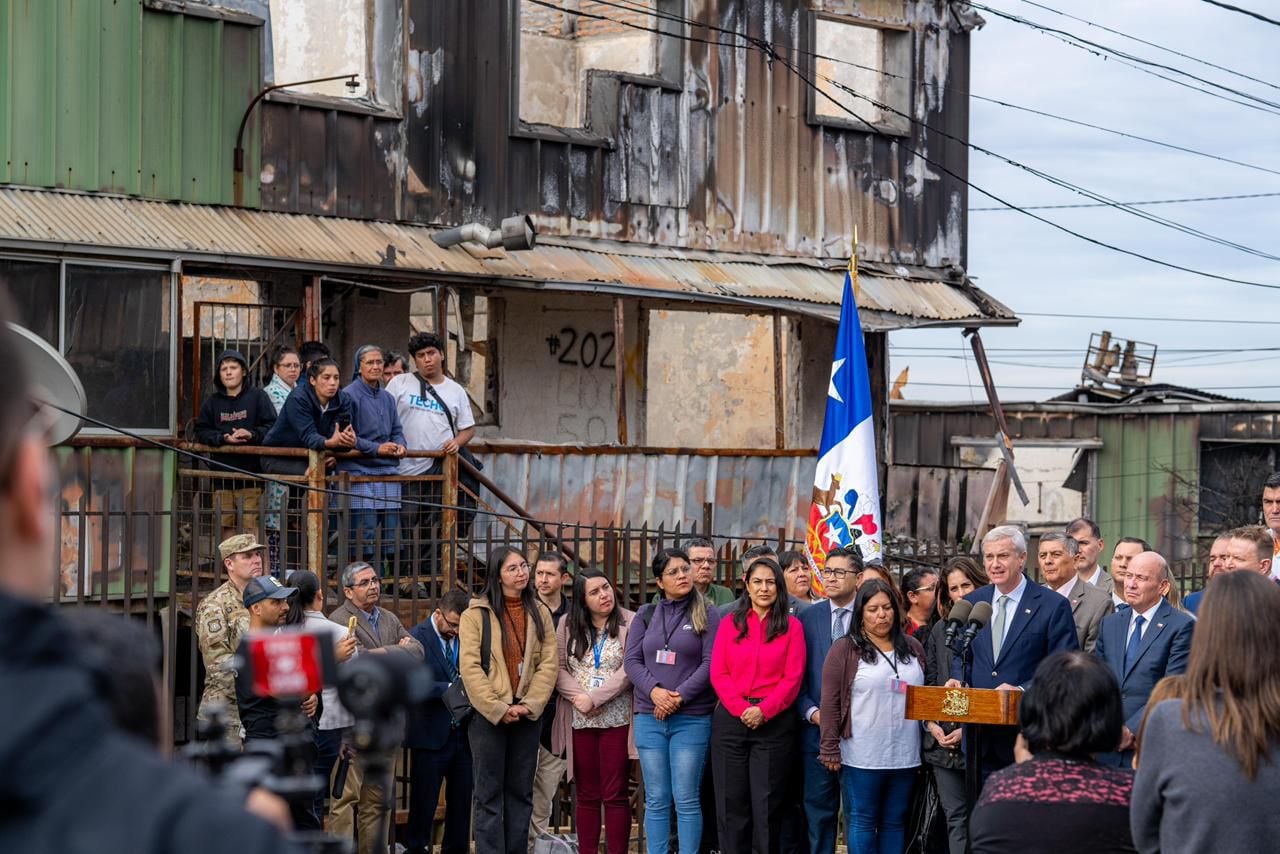 Punto de prensa oficial frente a viviendas dañadas. Vecinos observan desde los edificios siniestrados.