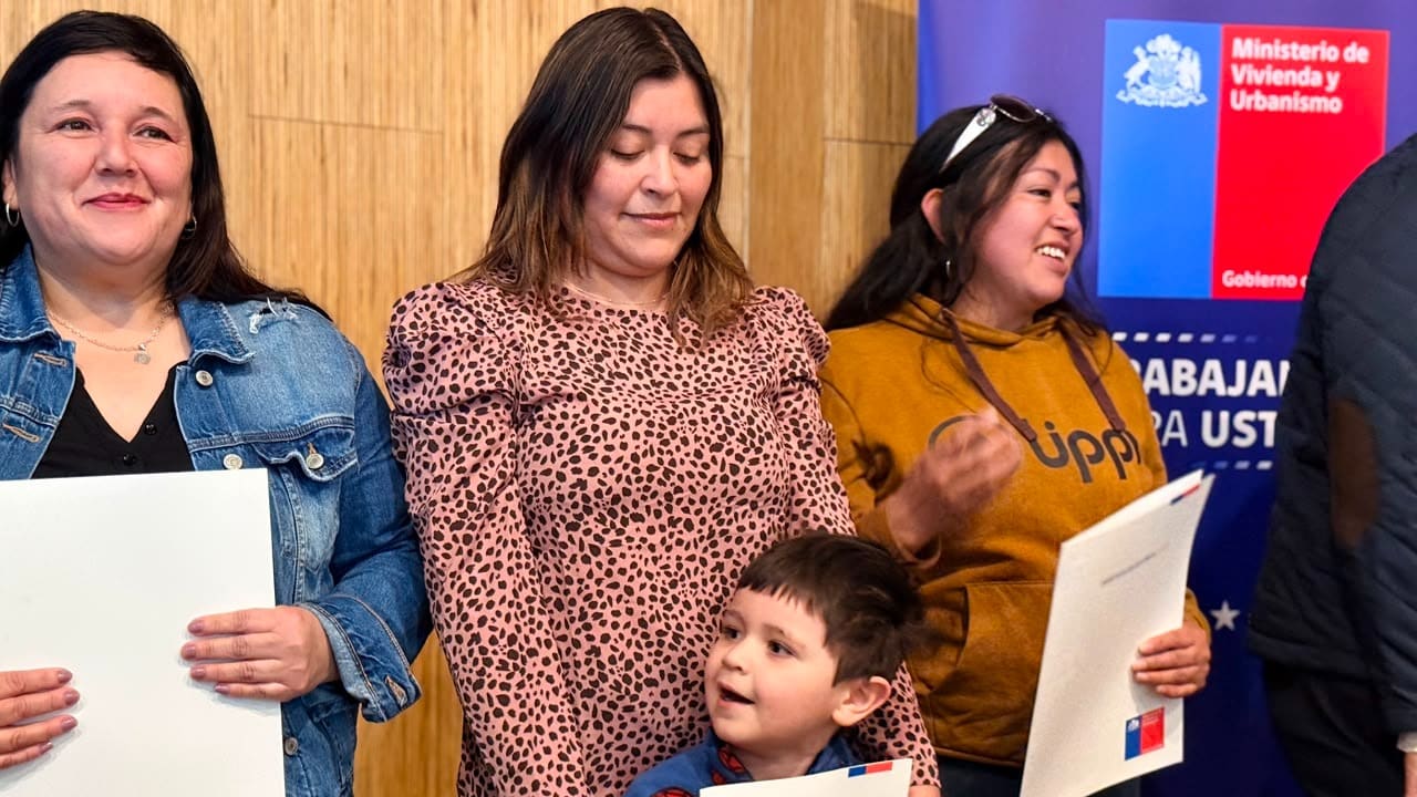 Familias de Frutillar sostienen las carpetas con la escritura de sus viviendas durante la ceremonia en la Biblioteca Municipal