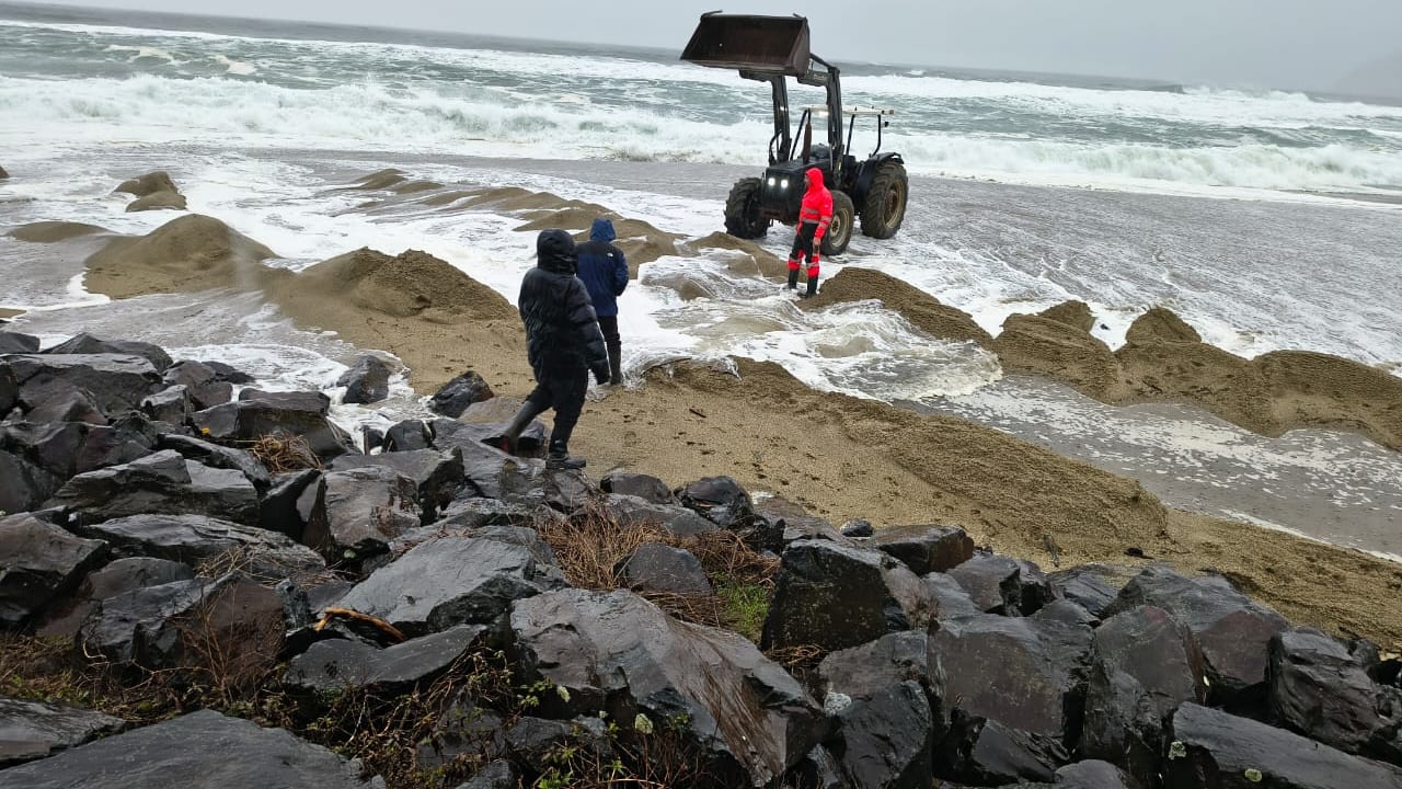 Un tractor y trabajadores intentan abrir la barra del río Llesquehue en la playa de Pucatrihue, entre marejadas, en San Juan de la Costa