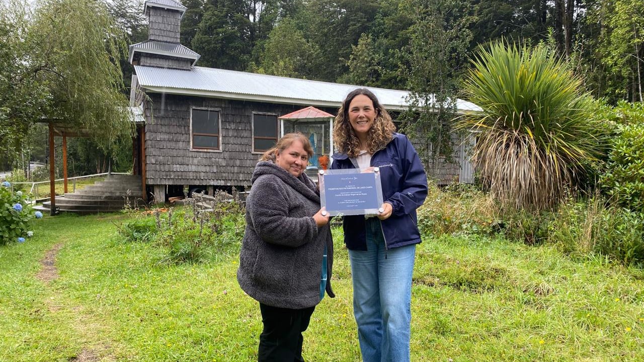 Dos representantes de una organización comunitaria de Lago Chapo reciben el reconocimiento del fondo frente a la capilla del sector