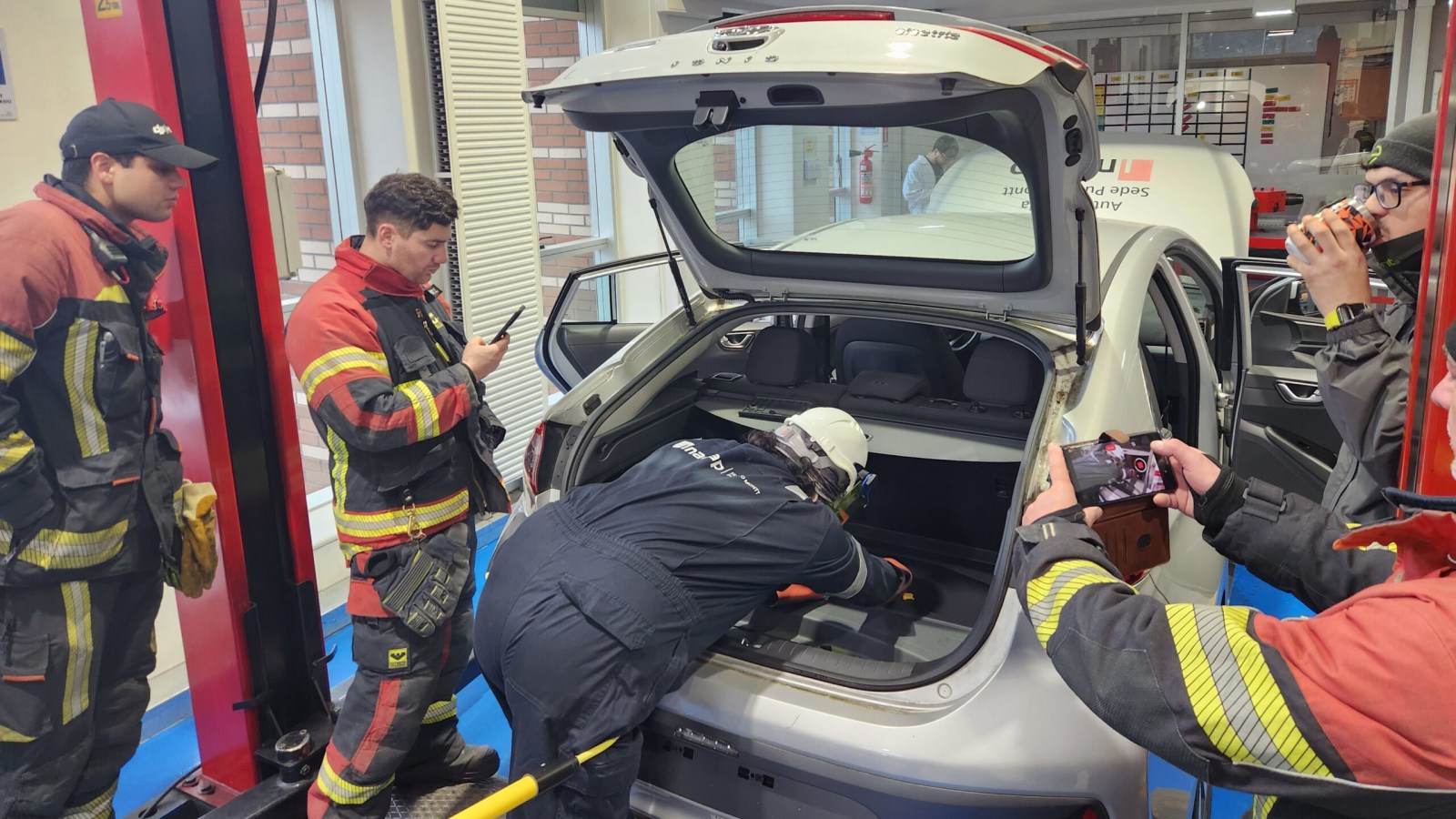 Voluntarios de Bomberos y un instructor de INACAP trabajan sobre el maletero abierto de un auto eléctrico durante la capacitación