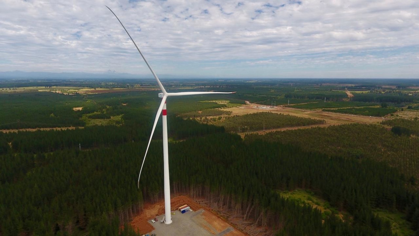 Vista aérea de un aerogenerador en operación rodeado de bosque de pinos y campos, en la Región de Los Lagos