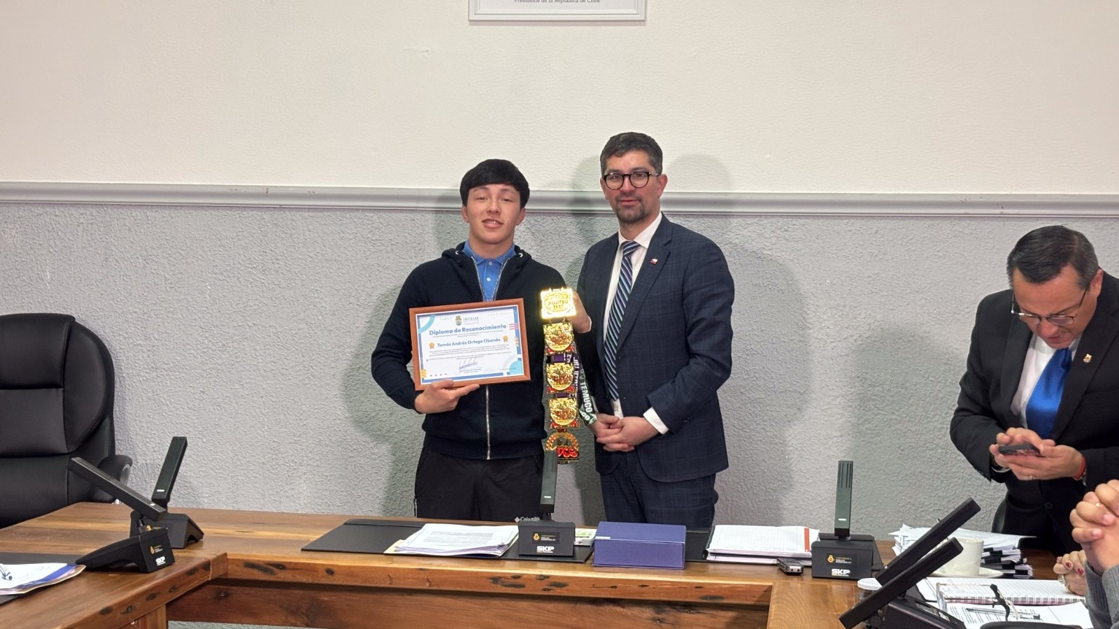 Tomás Ortega recibe su diploma de reconocimiento de manos del alcalde Javier Arismendi en la sala del Concejo Municipal de Frutillar