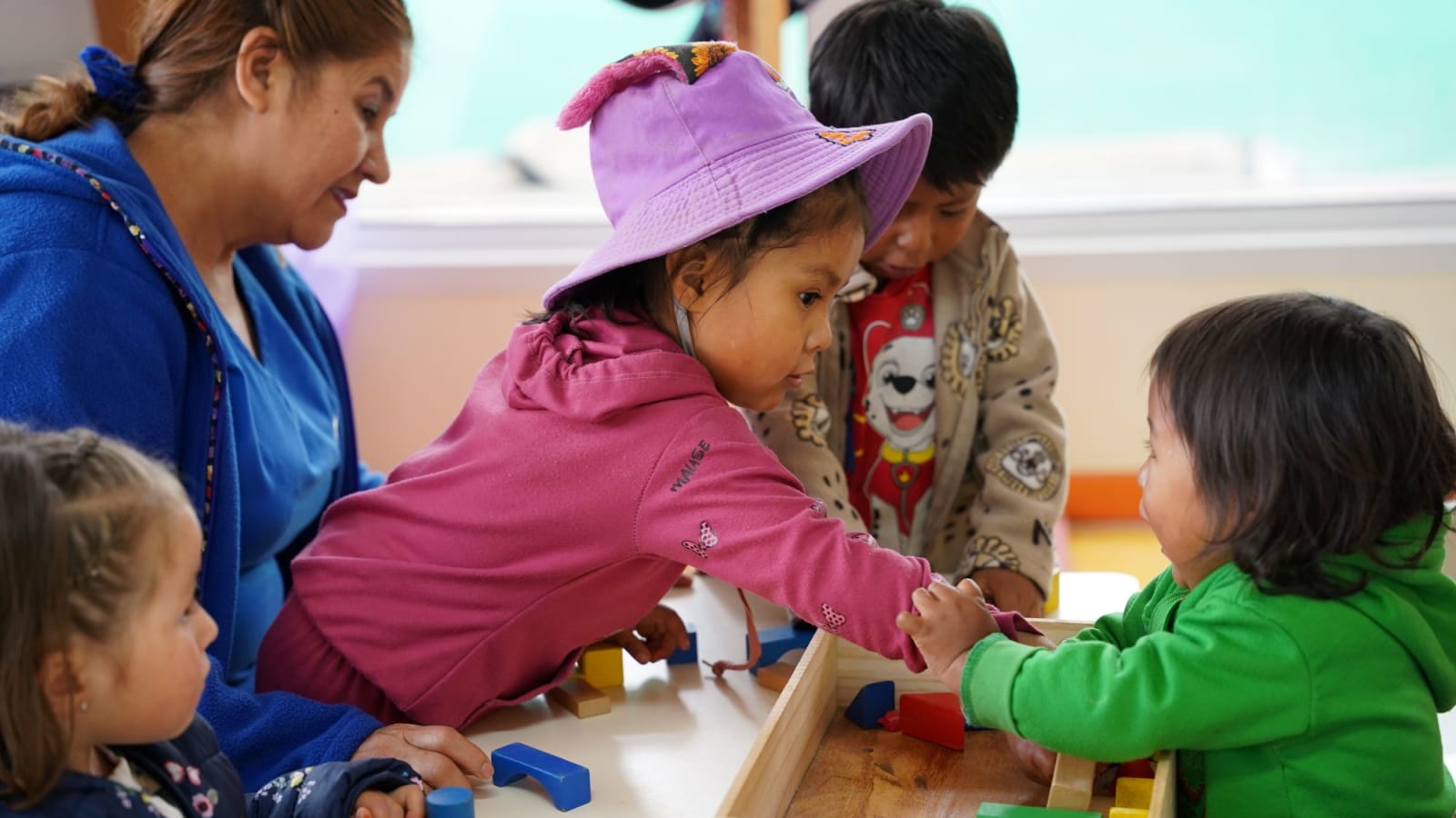 Una educadora y cuatro niños juegan con bloques de madera en una sala de jardín infantil