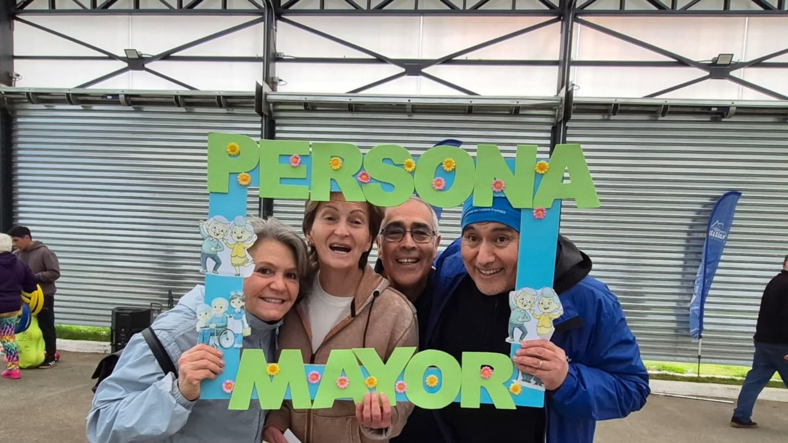 Cuatro personas mayores sonríen sosteniendo un marco que dice «Persona Mayor» en la Calle Techada de Frutillar