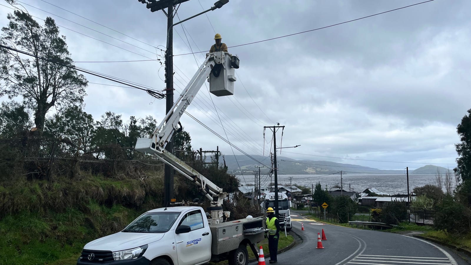 Cuadrilla de Saesa trabaja con un camión alza hombre en el tendido eléctrico junto a un camino de Chiloé