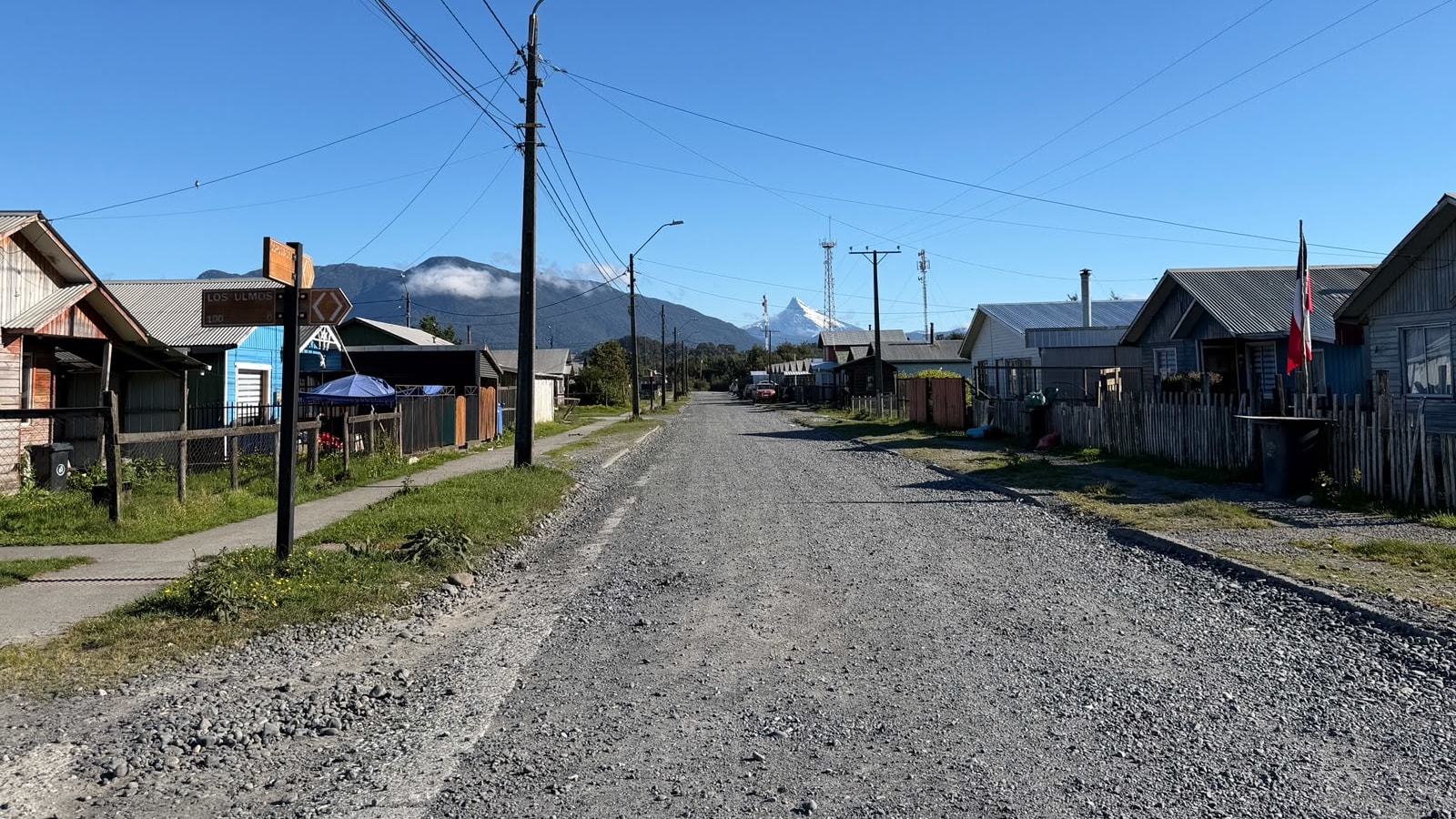 Calle de ripio en el sector sur de Chaitén, con el letrero de calle Los Ulmos y la cordillera nevada al fondo
