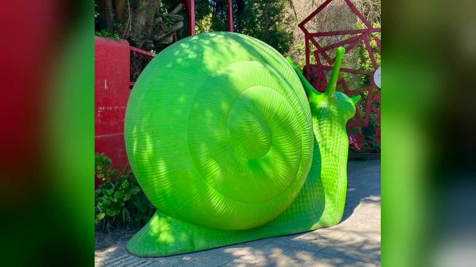 Caracol gigante de color verde del colectivo Cracking Art, hecho de plástico reciclado, en un jardín