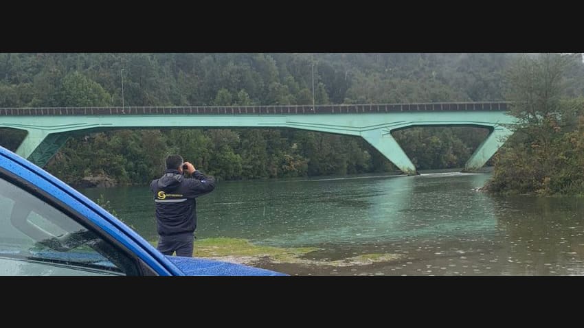 Fiscalizador de Sernapesca observa con binoculares un río de la Región de Los Lagos junto a un puente durante la temporada de pesca recreativa