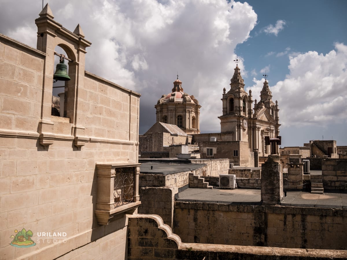 The dome and bell towers of Mdina Cathedral rising above the city's limestone bastion walls under a cloudy sky