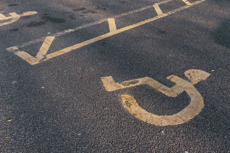 Yellow-painted accessible parking symbol and marking on dark asphalt pavement.