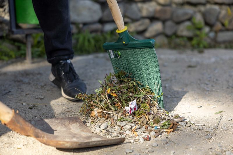 Person raking leaves into a green dustpan on a stone path outdoors