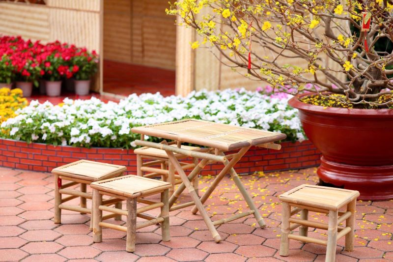 Small wooden table and stools in a courtyard garden with red and white flowers.