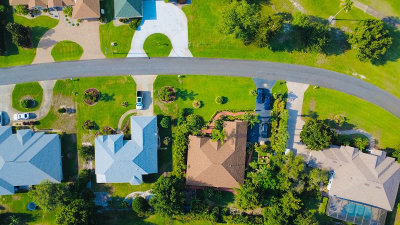 Aerial view of suburban houses with driveways, lawns, and a curved road surrounded by trees.