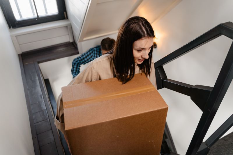 Woman carrying a large cardboard box up a staircase in a stairwell