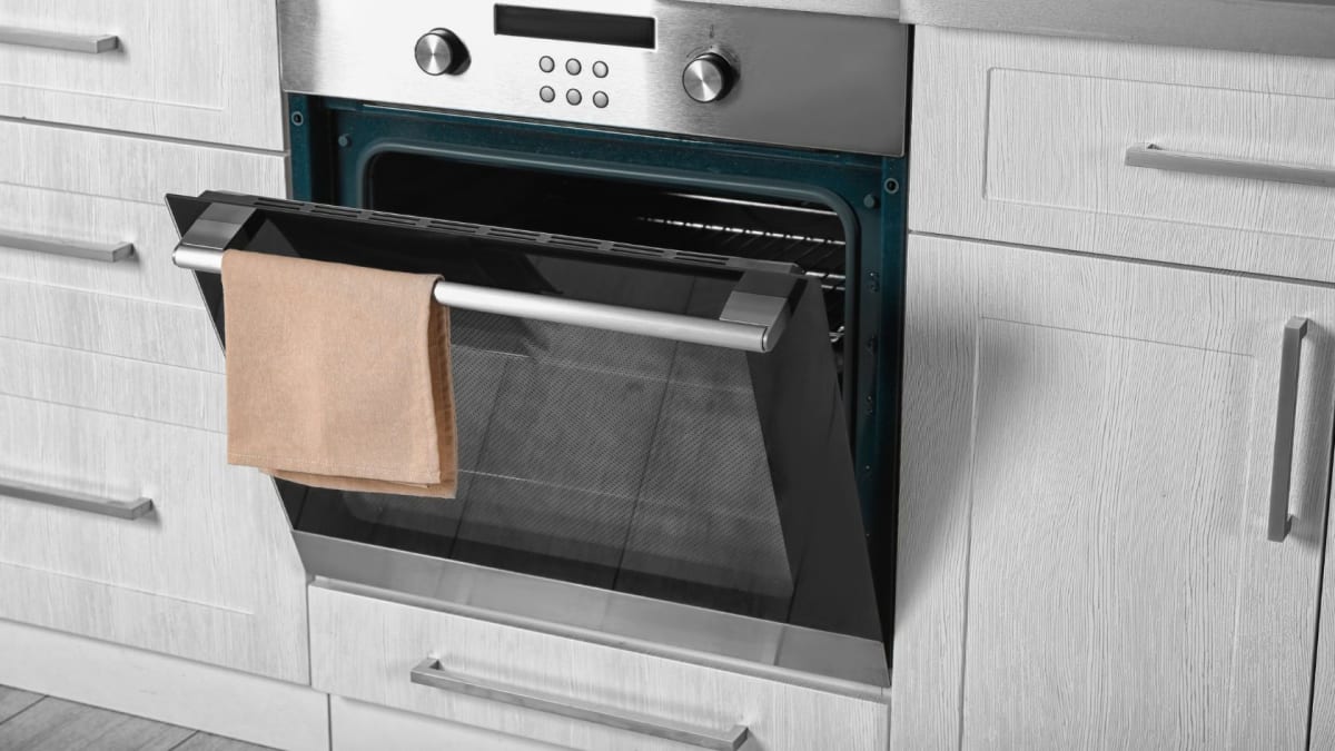 Open oven with a tan towel hanging on the handle, set in a white kitchen.