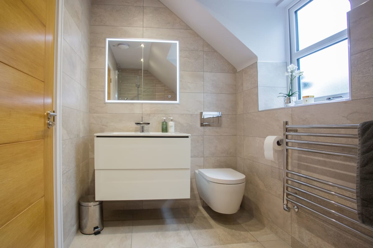Modern beige bathroom with vanity, mirror, wall-mounted toilet, towel warmer, and window