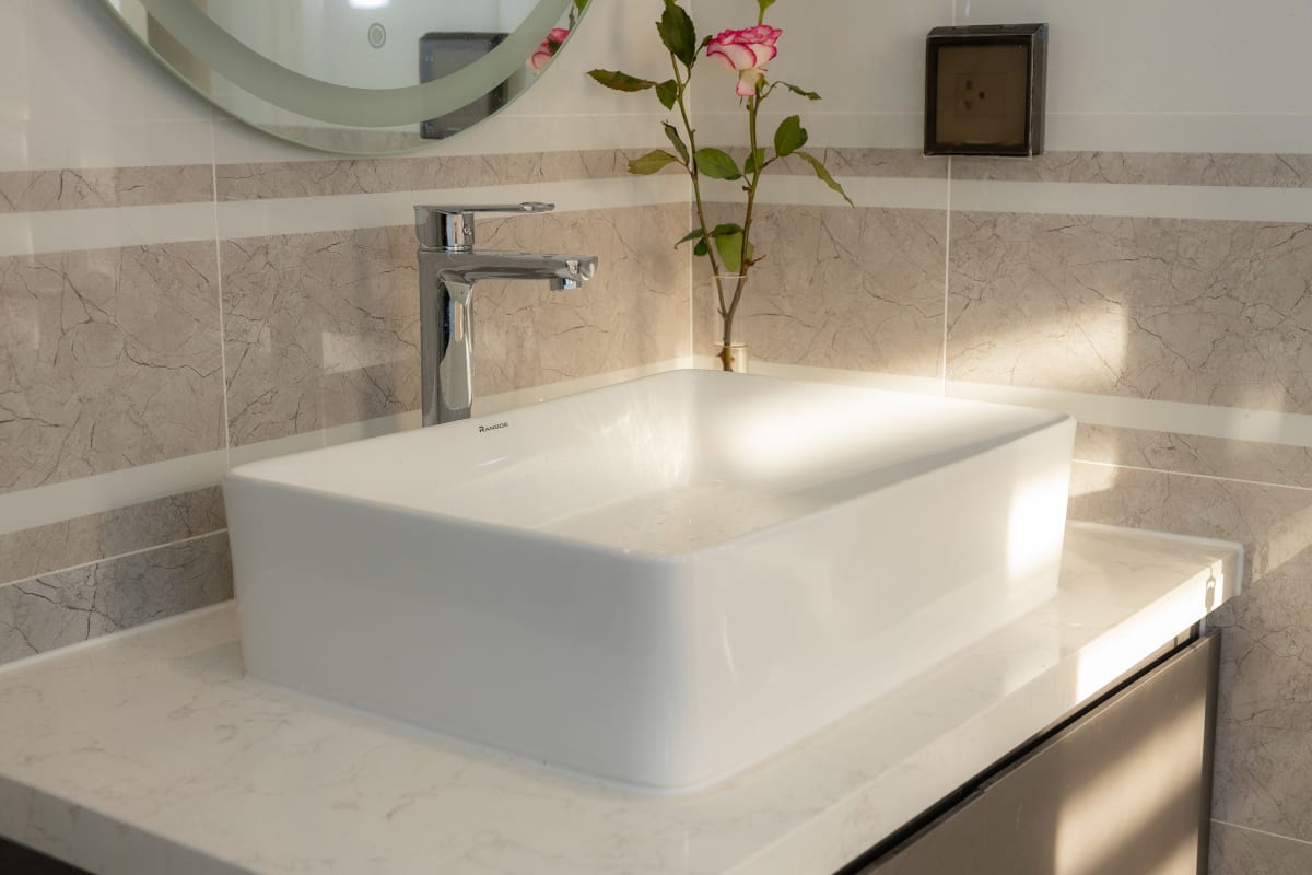 Modern bathroom with a white countertop sink, chrome faucet, mirror, and a small vase of flowers
