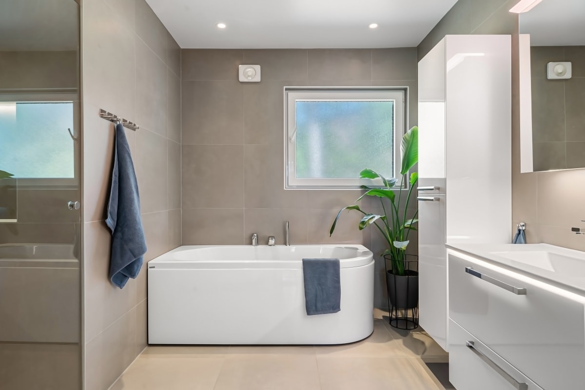 Modern bathroom with freestanding tub, gray tile walls, white vanity, and a small window