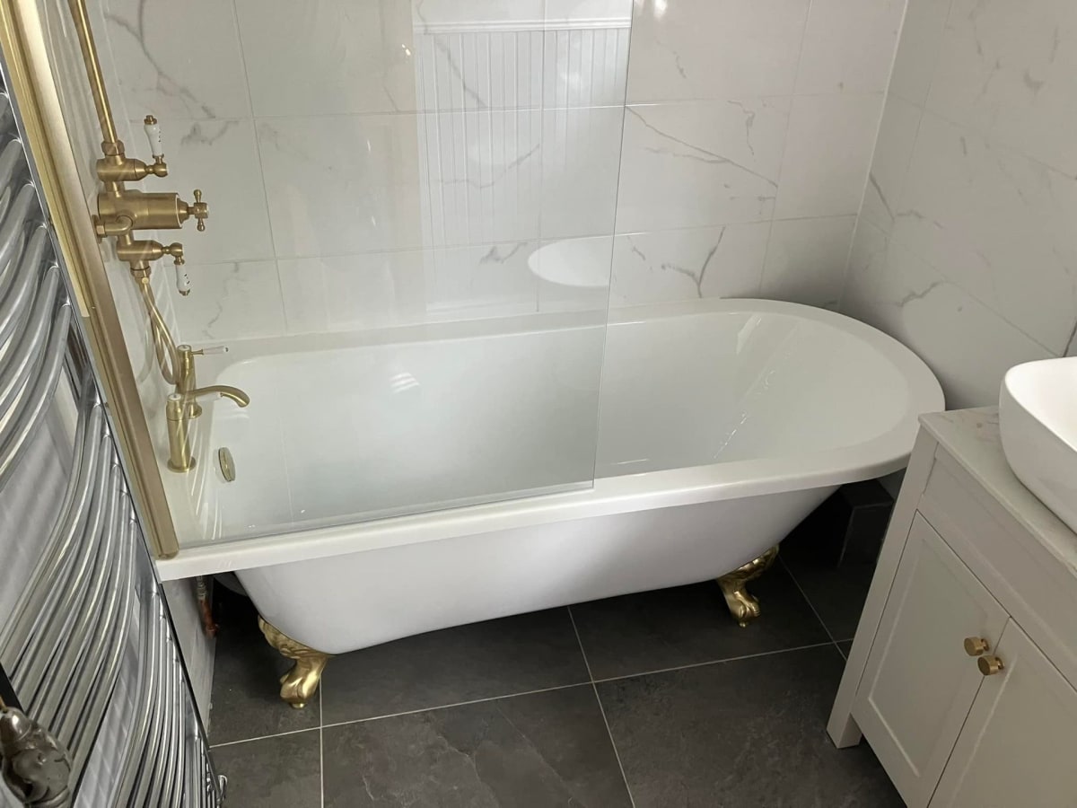 White clawfoot bathtub with gold fixtures in a marble-tiled bathroom.