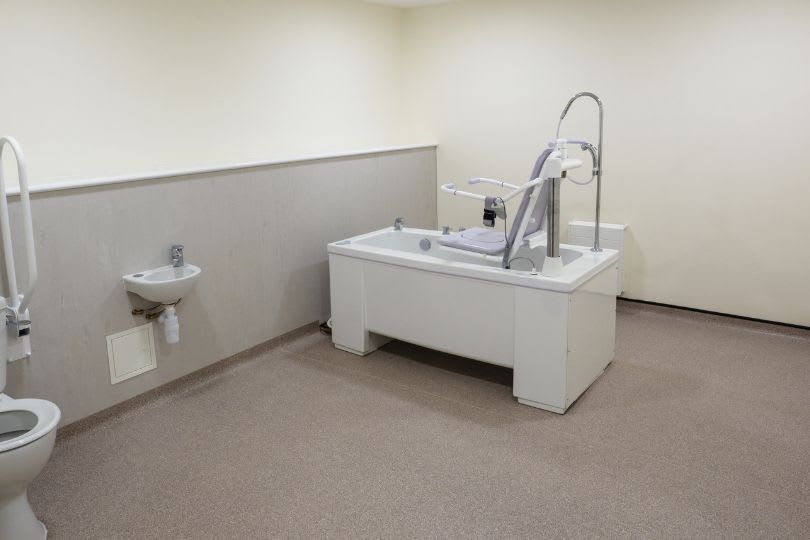 Empty clinic exam room with a sink, toilet, and a white medical exam table