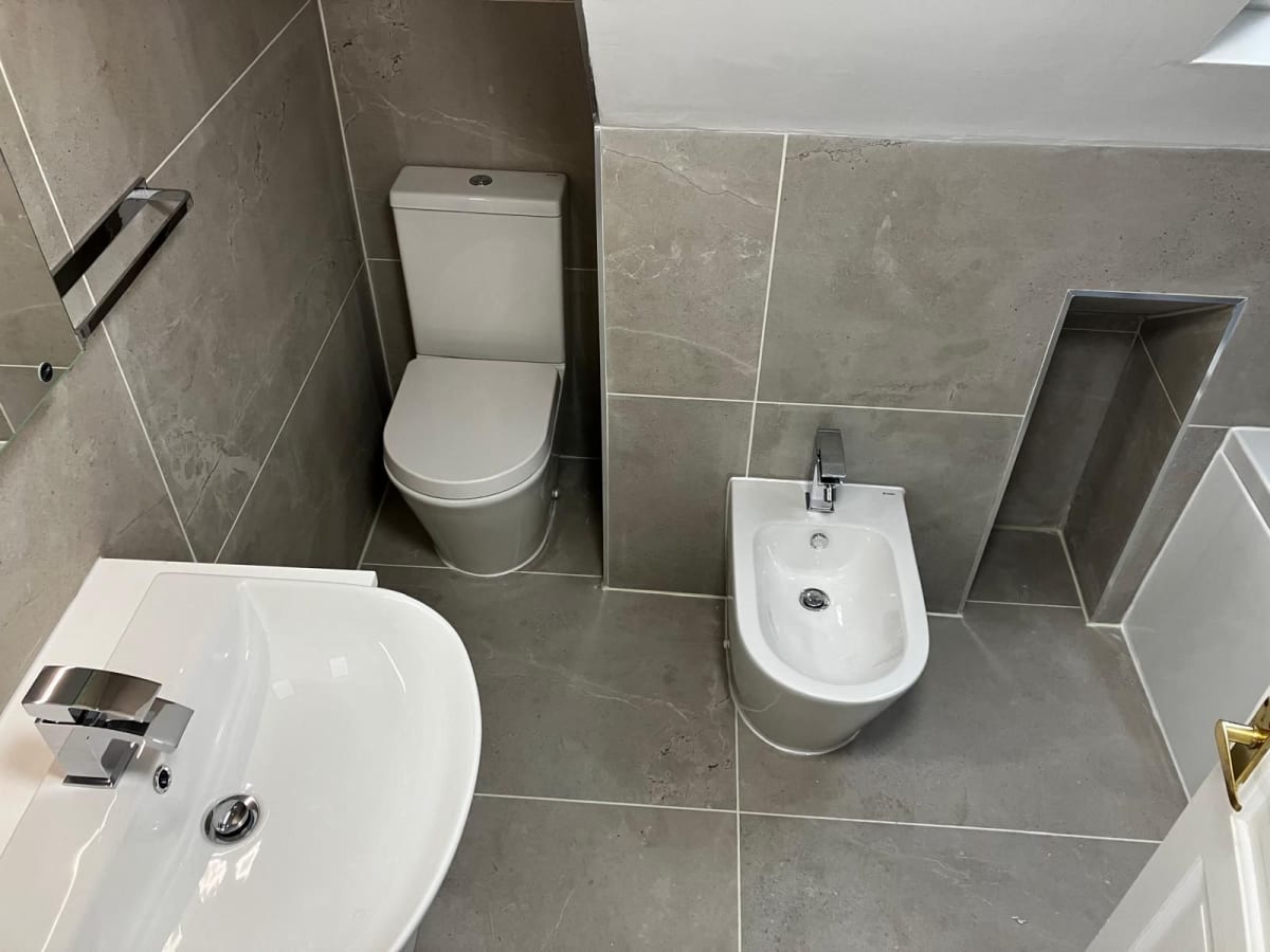 Modern gray-tiled bathroom with toilet, sink, bidet, and walk-in shower area