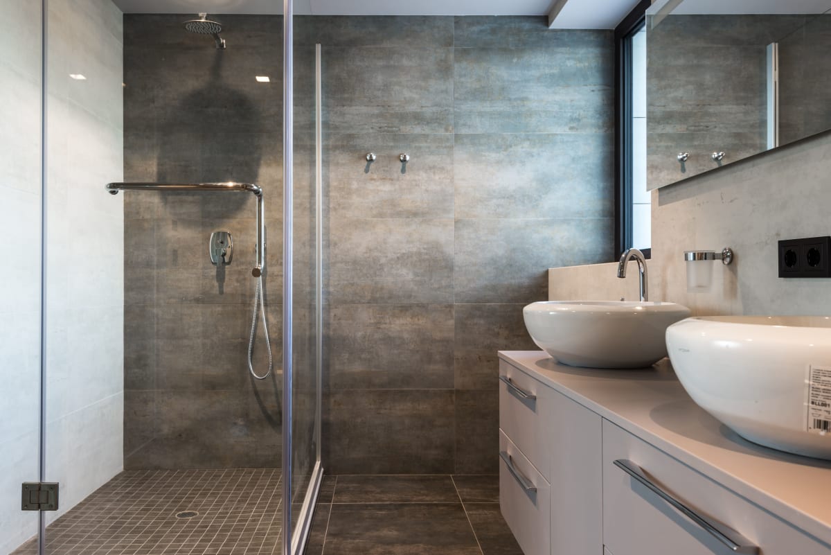 Modern bathroom with walk-in shower, double sinks, gray tile, and glass partition
