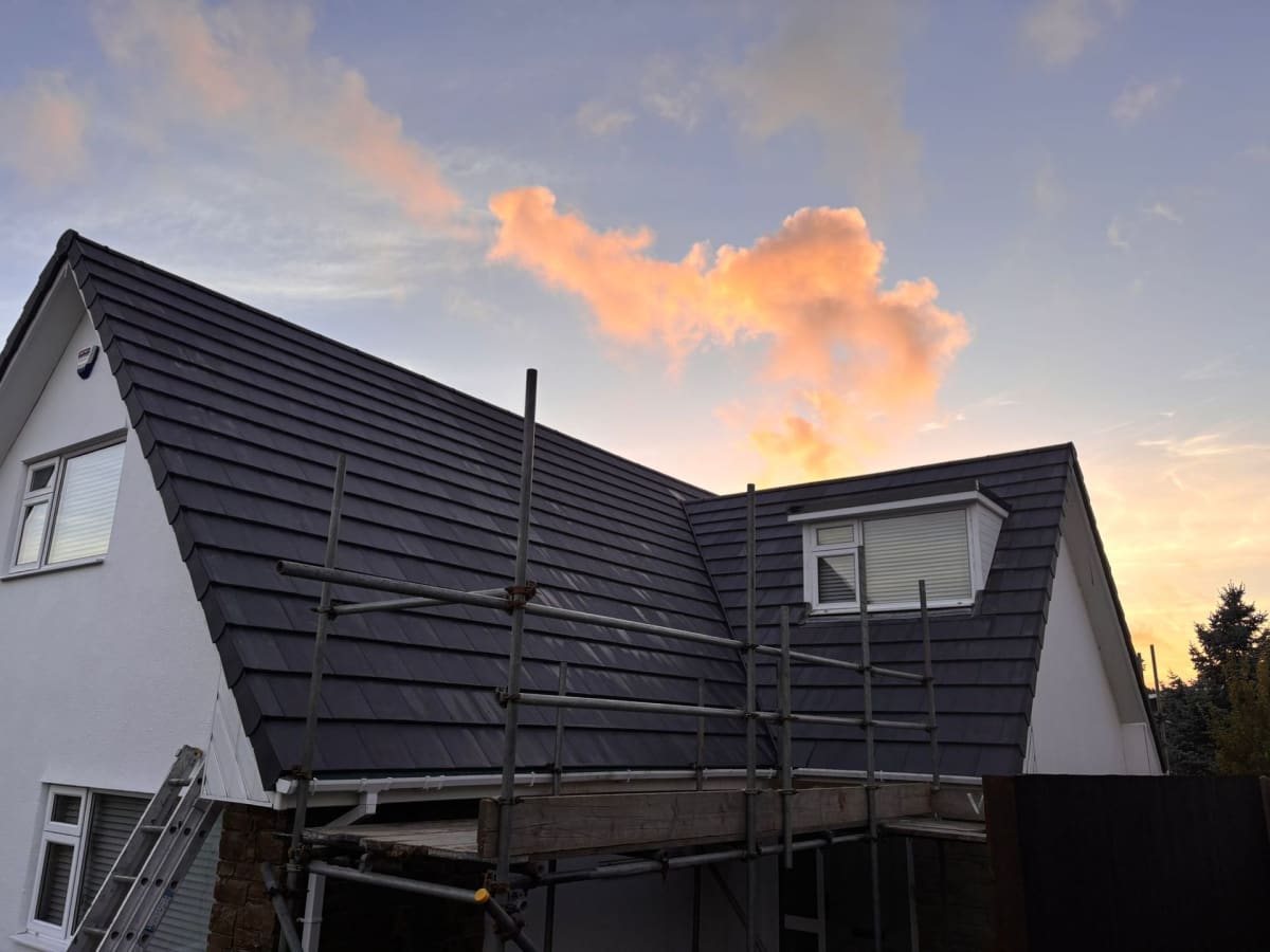 House with dark roof under construction, fronted by scaffolding at sunset