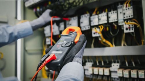 Person testing electrical panels with a digital multimeter in a wiring cabinet