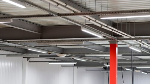 Industrial ceiling with exposed ducts, lights, and a red support column in a warehouse-like interior