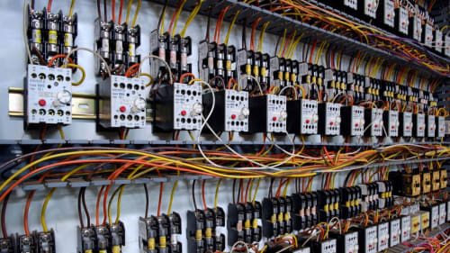 Electrical control panels with rows of switches, wiring, and circuit components in an industrial setting