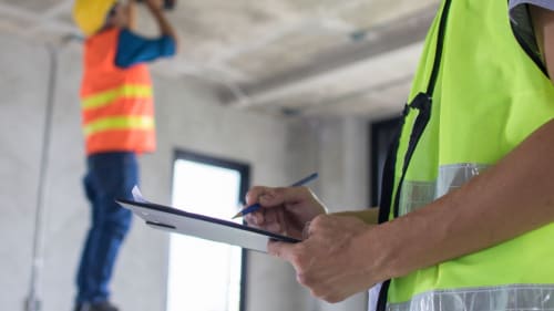 Construction worker in a neon vest taking notes on a clipboard at an indoor job site