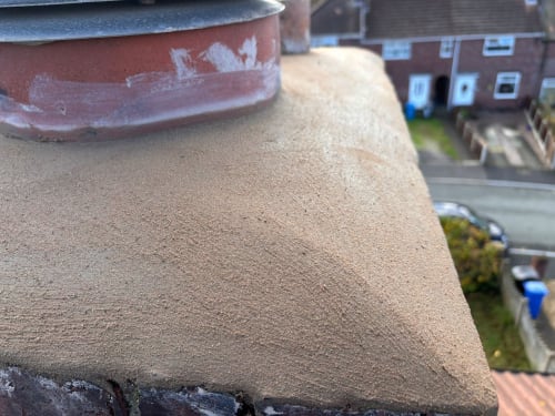 A close-up view of a newly pointed chimney crown, showing textured tan mortar sloped around a terracotta chimney pot.